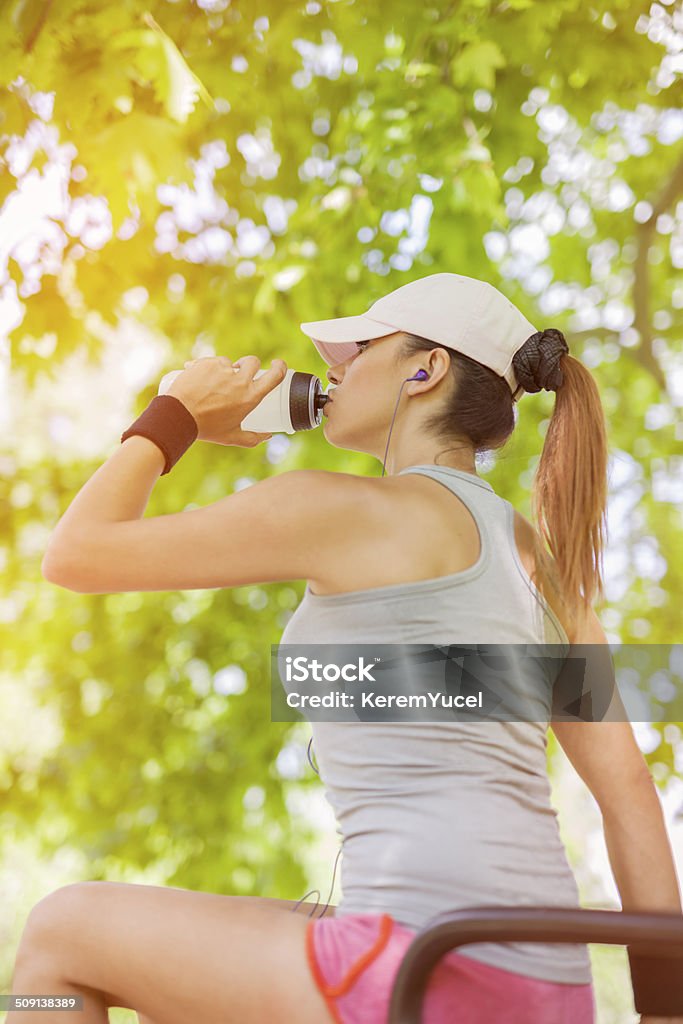 thirsty young woman drinking water while sitting Young woman drinking water and listening to the music while resting. There is selective focus on the model. Activity Stock Photo