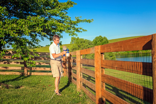A man is staining wooden fence with electric sprayer