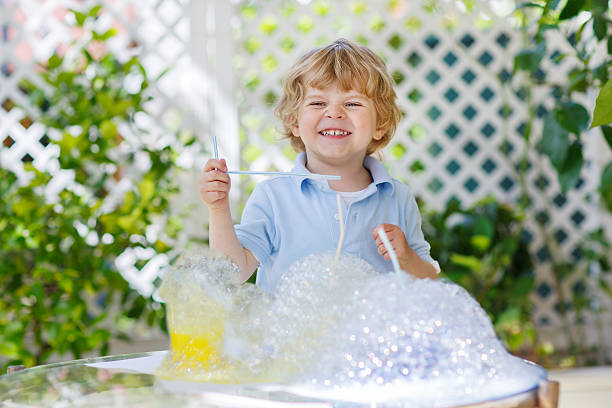 Happy little boy making experiment with colorful water and soap