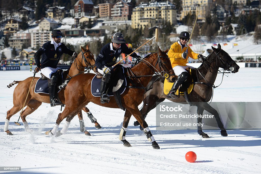 "Snow Polo World Cup St. Moritz" St.Moritz, Switzerland - January 30. 2016: Two players from the team Badrutt's Palace Hotel in dark blue polo shirt, against a player from the team Perrier-Jouet Polo in yellow, play polo on the frozen Lake St. Moritz. In the background are some houses of St. Moritz. The "Snow Polo World Cup St. Moritz" is the most prestigious winter polo tournament on snow. Four high-goal teams with handicaps 15 to 18 goals on the frozen Lake St. Moritz to fight for the win. The picture was taken on Saturday at the Polo game 3. The tournament will run from Thursday to Sunday. The image was taken at the edge of the field to the frozen lake. Input on the frozen lake of St. Moritz is free and attracts thousands of spectators. Horse Stock Photo