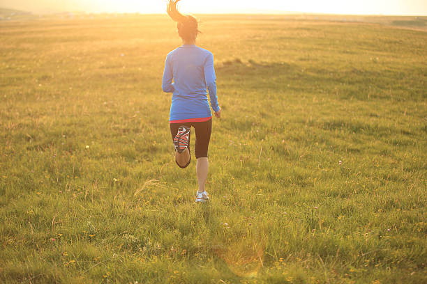 Runner athlete  running on sunrise/sunset grass field. woman fitness jogging workout wellness concept.