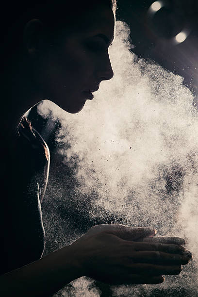 Young woman applying sports chalk on her hands Silhouette of a young fit woman standing in a cross training rack, applying magnesium gym chalk on her hands. crossfit chalk weightlifting weight training stock pictures, royalty-free photos & images