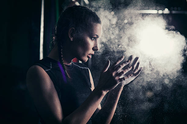 Young woman applying sports chalk on her hands Silhouette of a young fit woman standing in a cross training rack, applying magnesium gym chalk on her hands. crossfit chalk weightlifting weight training stock pictures, royalty-free photos & images