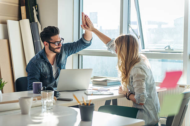 Success in business Two happy coworkers high-fiving each other after a well done job. office fun business adhesive note stock pictures, royalty-free photos & images