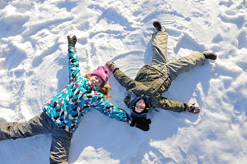 Girl and boy lying on snow at winter weather