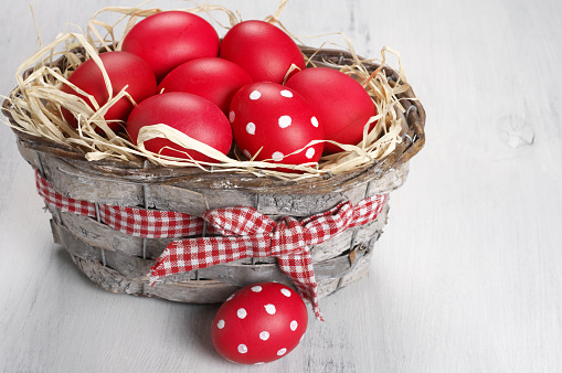 Traditional red and dotted Easter eggs in gray basket on rustic wood background.