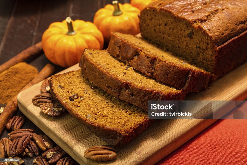 Pumpkin Bread Sliced pumpkin bread loaf sitting on wooden cutting board with pecan nuts and cinnamon spices Pumpkin Bread Stock Photo