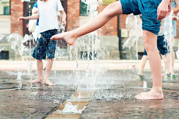 Summertime enjoyment. Kids legs and feet wet in fountain. Outdoors.