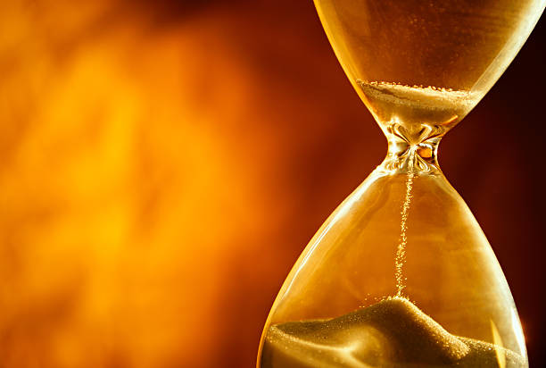 Sand passing through the bulbs of an hourglass Sand passing through the glass bulbs of an hourglass measuring the passing time as it counts down to a deadline or closure on a yellow background with copyspace hourglass stock pictures, royalty-free photos & images