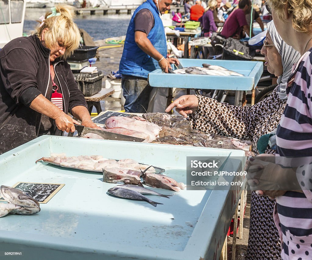 Fishermen sells fresh fish at Old Port of Marseille Marseille, France - August 24, 2014: Fishermen sells fresh fishes at Vieux Port. Many fishes on tables. Mature woman cutting big tuna on foreground. Many people watching and choosing fishes Marseille Stock Photo