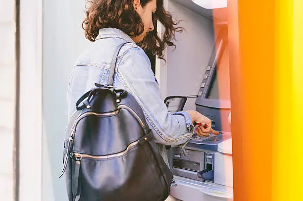Woman using credit card withdrawing money from an ATM machine outside a branch of savings bank.