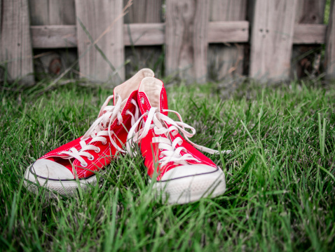 close up of red sneakers in green grass with a wooden fence in the background
