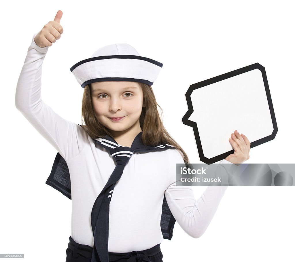 Sailor Girl with Speech Bubble Portrait of happy little girl dressed as a sailor holding speech bubble next to her head and raising her hand with thumb up. Studio shot, isolated on white. 6-7 Years Stock Photo
