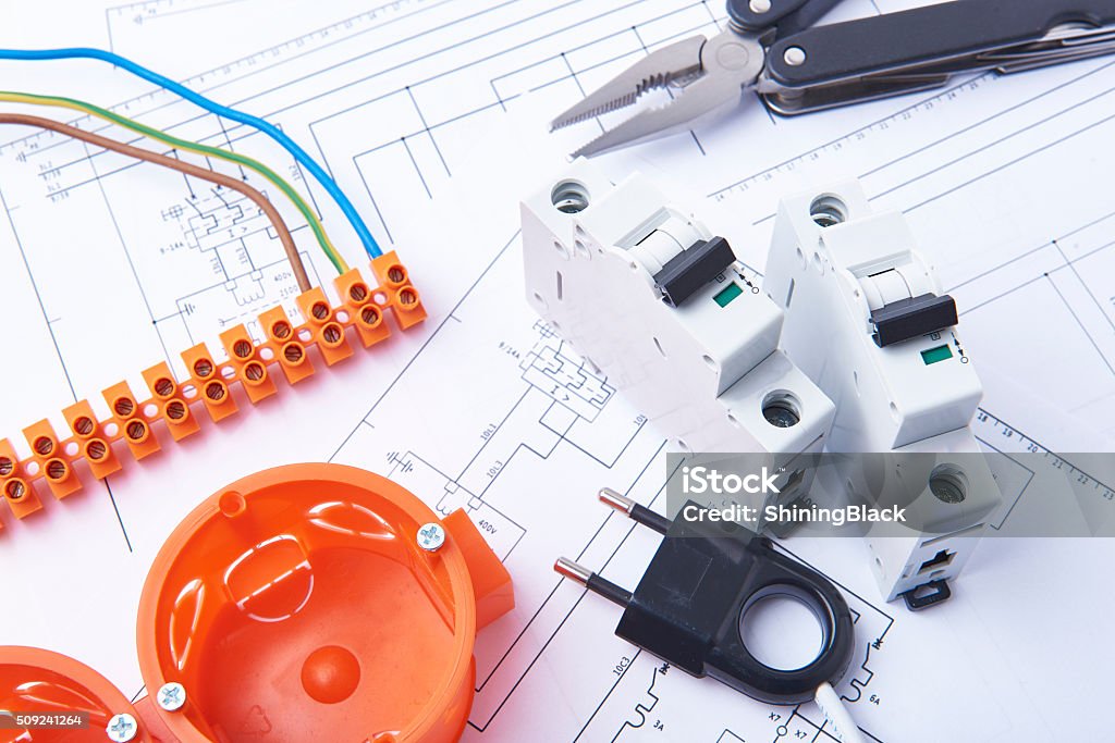 Electrical fuses and materials used for jobs in electricity. Electrical connectors with wires, junction box and different materials used for jobs in electricity. Many tools lying on diagrams. Concept of electrical works. Plan - Document Stock Photo