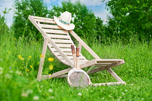 Chaise-longue with a hat and badminton rackets in the middle of the meadow.