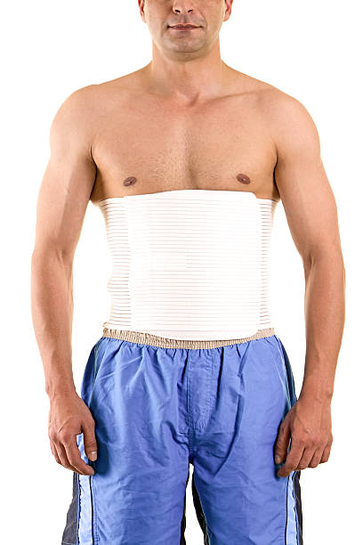 Shirtless Man Wearing Brace to Support Core. Shirtless Man in Studio with White Background Wearing Orthopedic Brace to Support Core and Lower Back. feldspar stock pictures, royalty-free photos & images