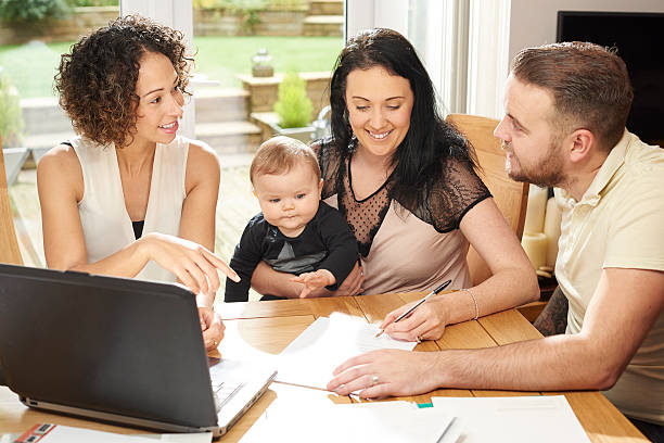 financial advisor gets the signature a young husband and wife with their baby sit and chat to a woman in their dining room . They are all referring to a laptop in front of them and various paperwork is dotted about the table. unknown gender stock pictures, royalty-free photos & images