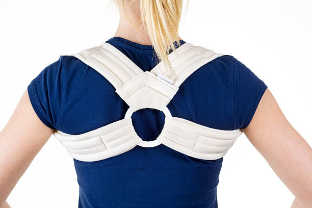 Blond Woman Wearing Supportive Back Brace. Close Up Rear View of Blond Woman in Blue T-Shirt Wearing Supportive Orthopedic Back and Shoulder Brace in Studio with White Background. clavicle stock pictures, royalty-free photos & images