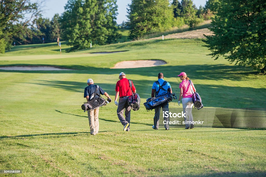 Golfers Walking On The Golf Course Four golfers walking on the golf course. Rear View.  Golf Stock Photo