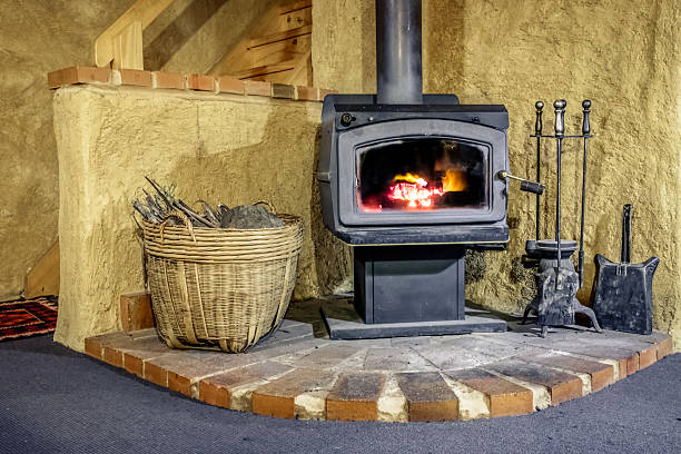 Wood Fired Stove in Mudbrick Cottage A wood fired stove with a fire burning, with a basket of wood and fireplace brush, poker and spade. Located in an adobe mudbrick cottage. adobe oven stock pictures, royalty-free photos & images