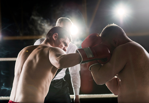 In the boxing ring, two boxers are fighting while the referee is in the background.   