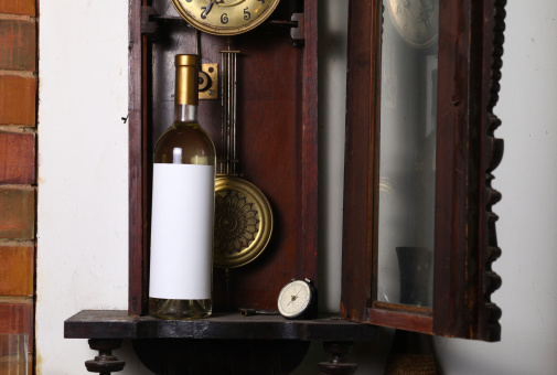 Bottle of white wine with blank label template standing inside an old clock