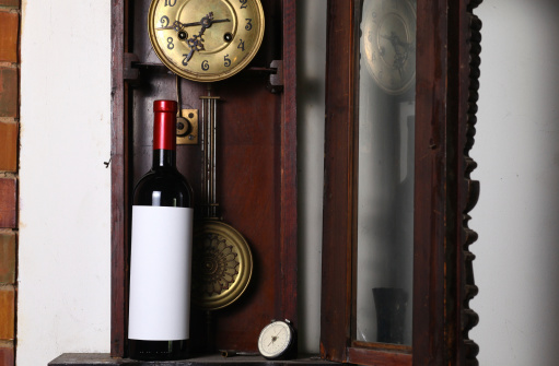 Bottle of red wine with blank label template standing inside an old clock