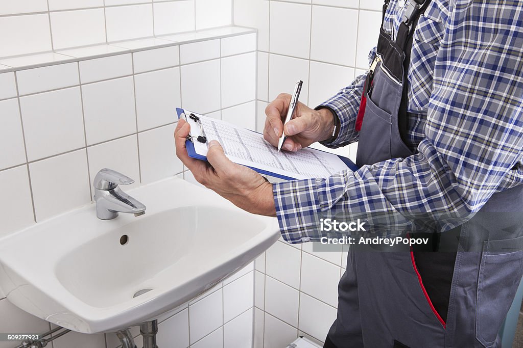 Plumber Standing In Front Of Washbasin Writing On Clipboard Close-up Of Plumber Standing In Front Of Washbasin Writing On Clipboard Bathroom Stock Photo