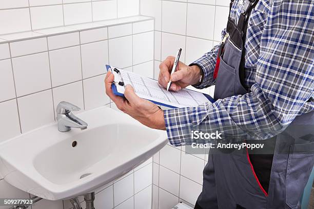 Plumber Standing In Front Of Washbasin Writing On Clipboard Stock Photo - Download Image Now