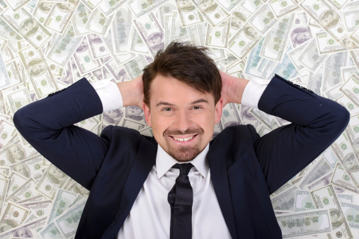 Young businessman resting upon money on a white background
