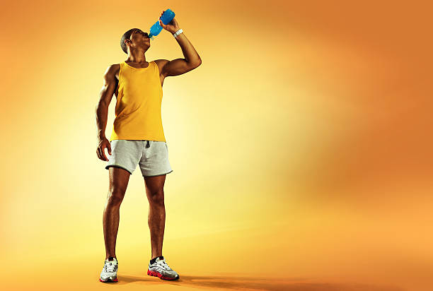 Sport. Young athlete drinking water of bottle after running Young muscular build man drinking water of bottle after running, attractive athlete resting after workout outdoors, fitness and healthy lifestyle concept. Isolated on yellow sport drink stock pictures, royalty-free photos & images