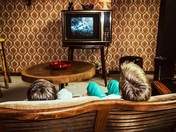 two boys watching television at home in 50's style, shot from behind