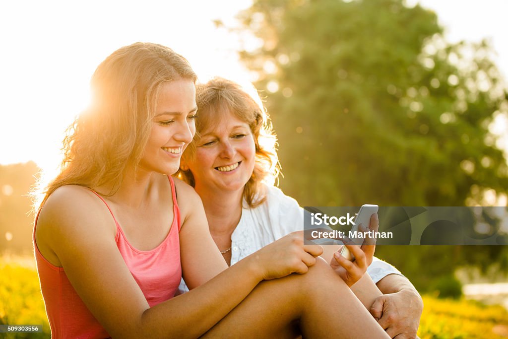 Happy moments together - mother and daughter Teenage girl showing her mother photos on mobile phone outdoor in nature with setting sun in background Life Events Stock Photo