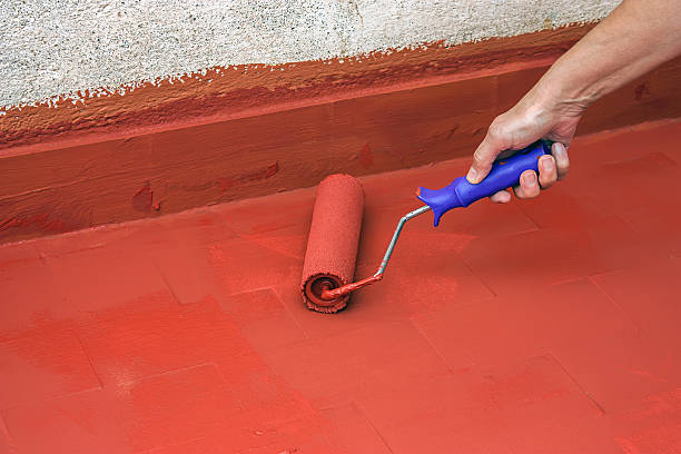 Hand painting a red floor with a paint roller stock photo