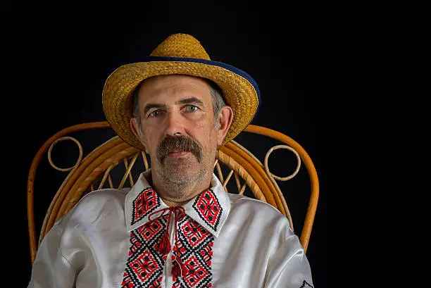 Portrait of Ukrainian country-man sitting in a wicker chair, wearing straw and traditional clothes (Vyshyvanka)