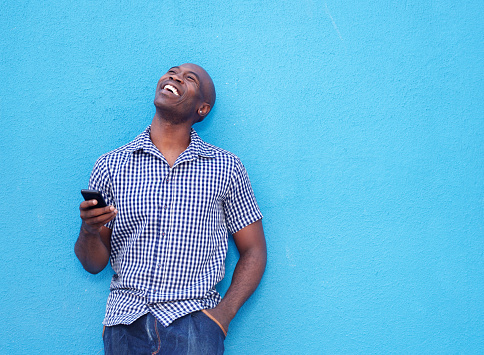 Portrait of smiling african man with a mobile phone standing against blue background