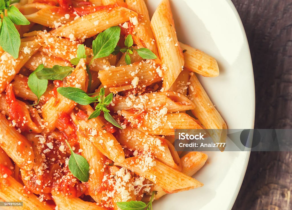 Penne pasta in tomato sauce Penne pasta in tomato sauce with basil and parmesan cheese on rustic wooden background. Penne Stock Photo