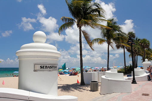 Fort Lauderdale, FL, USA - May 23, 2015: White pillar wall sign to Sebastian Street and SR A1A beach. People on the sunny beach at the end of Sebastian Street.