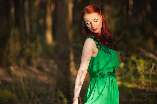 Beautiful red hair fairytale girl in green dress with face art