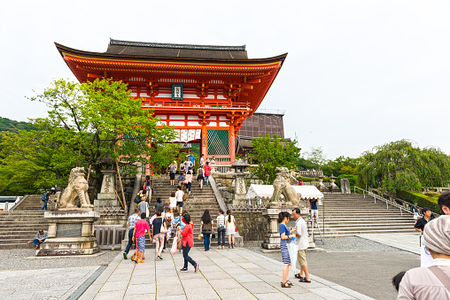 Kyoto, Japan - August 12, 2014: View on beautiful decorated Shinto temple, colored red, people walking up to the temple on staircase. Trees behing the temple. 