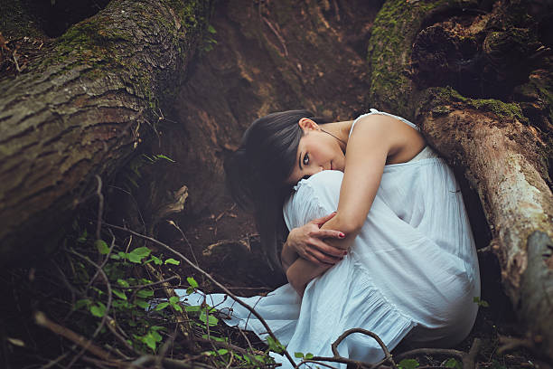 Beautiful woman among dark tree roots looks into camera . Mother earth embrace