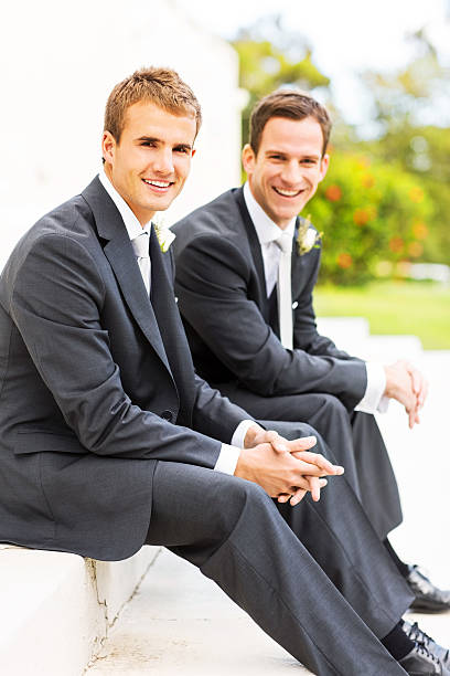 Best Man And Groom Sitting With Hands Clasped In Garden