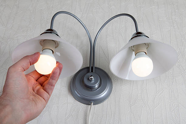 istock Hand twists led lightbulb in a lamp on white wall 509343118