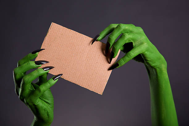 istock Green hands with long black nails holding cardboard 509343420