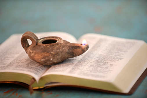 Ancient Israelite oil lamp on open Bible over vintage table