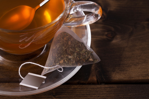 Fresh glass cup of tea with saucer and teabag close up. Set on a dark wooden table with space for text