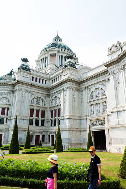Bangkok, Thailand - April 23, 2014: An Asian couple is visiting Ananda Samakhom Throne Hall and doin gsight seeing. Huge palace is one of landmarks of Bangkok. People are wearing hats as sun protection.