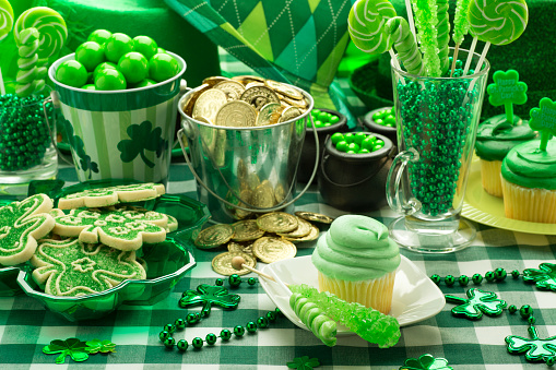 This is a close up photo of a St. Patricks Day Party with a green cupcake and a chcolate pot of gold on a checkered table cloth