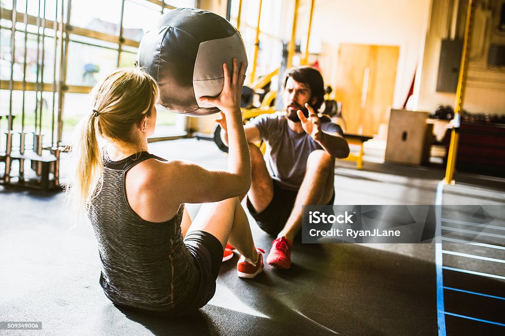 Ab Crunches with Medicine Ball A young couple does weighted crunches on the floor of a cross training gym, sunlight coming in from the windows behind them. Horizontal with copy space.  Gym Stock Photo