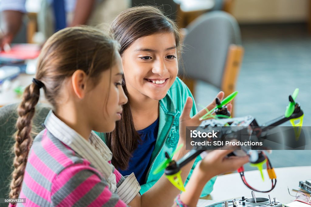 Elementary girls using drones during after school science program Elementary age Hispanic little girls are using drones during after school science club or program. Students are studying science, technology, engineering, and math in public elementary school library makerspace. Child Stock Photo